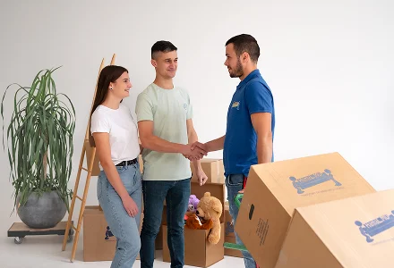 Clientul dă mâna cu un hamal în apartamentul pregătit pentru mutare, lângă cutii de carton