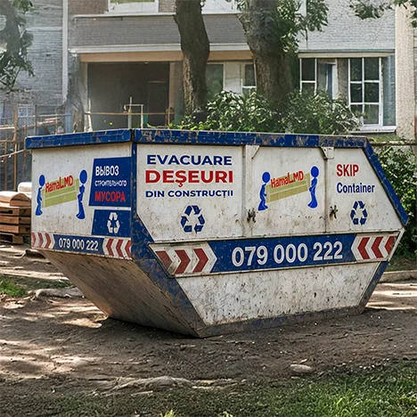 Container metalic cu marcaje pentru moloz, înconjurat de copaci lângă un bloc